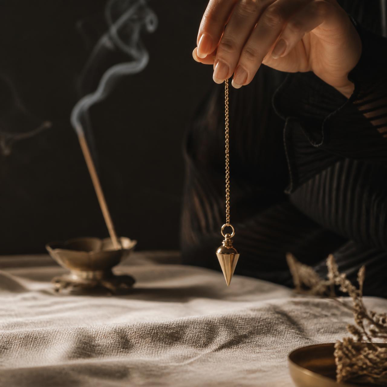 Brass pendulum held above linen with incense smoke